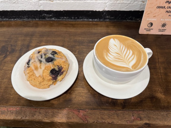 A picture of a blue berry muffin and latte on the table top of a cafe.